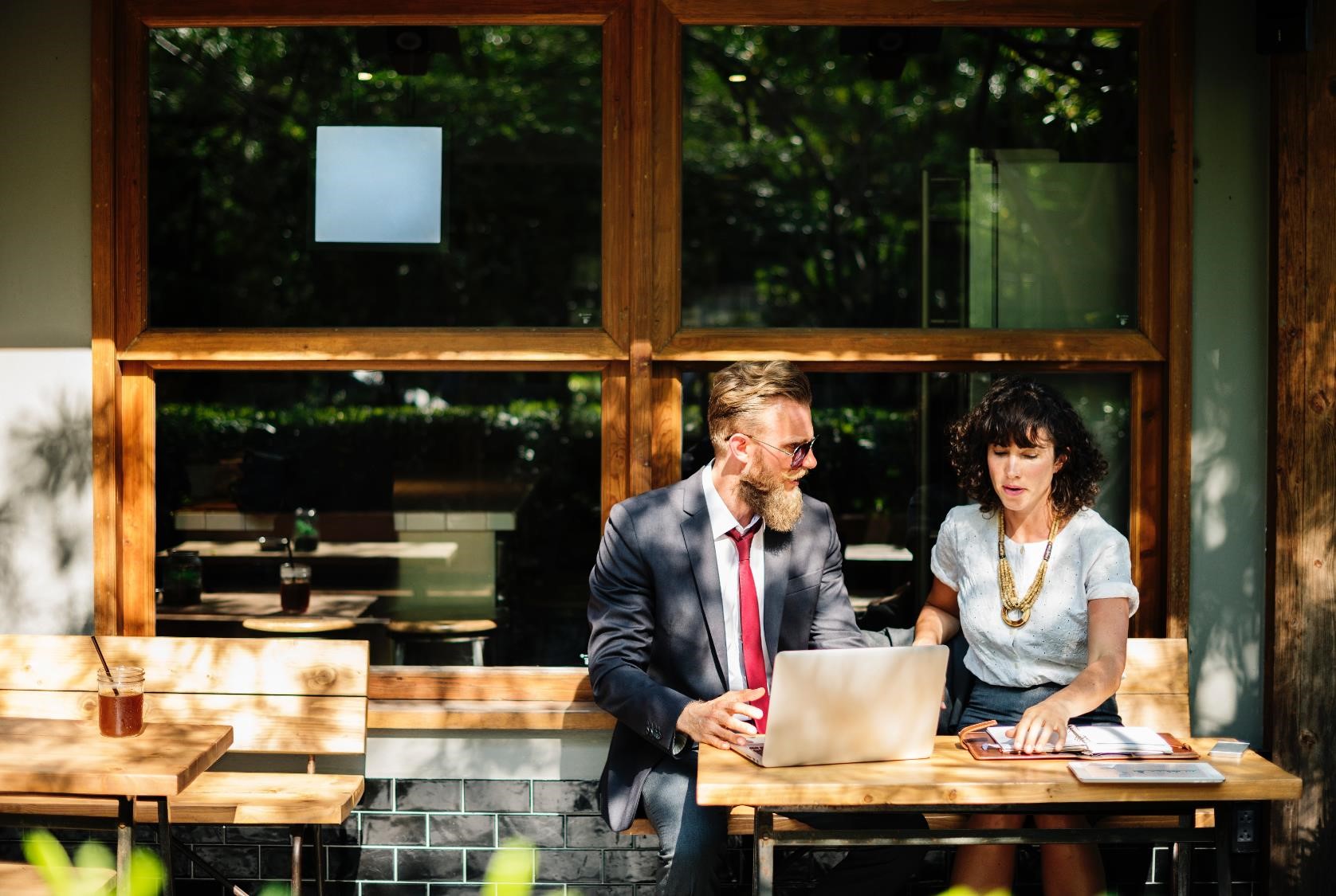 A man and a woman outside a cafe, looking at a computer and a notebook